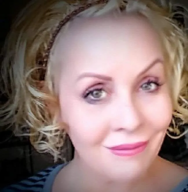 Teri Colby, smiling, with curly blonde hair and a braided headband.